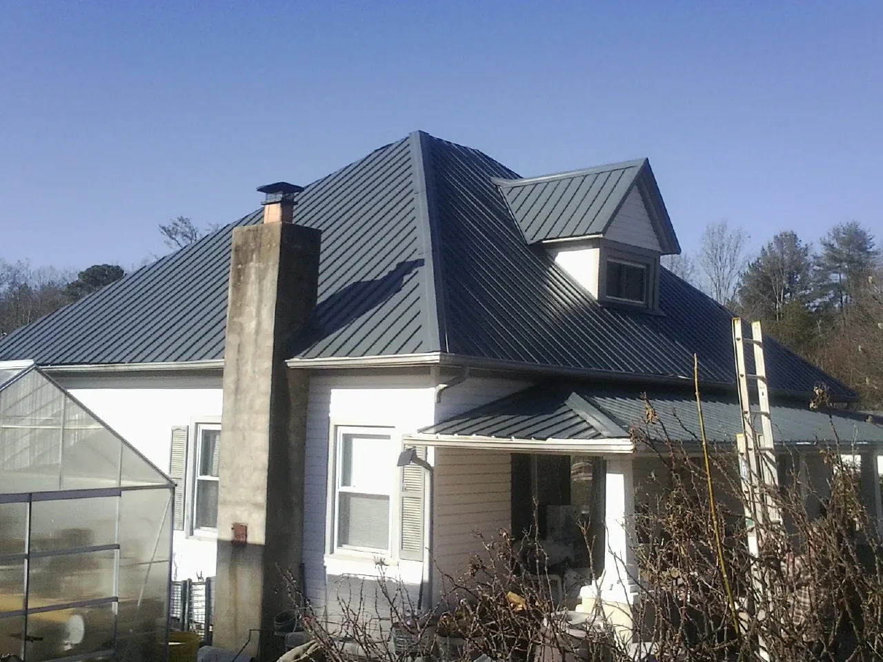 Dark blue standing seam metal roof on a white farmhouse with dormer — Slate & Tile Roof Repair by Roofing Brothers in Duson