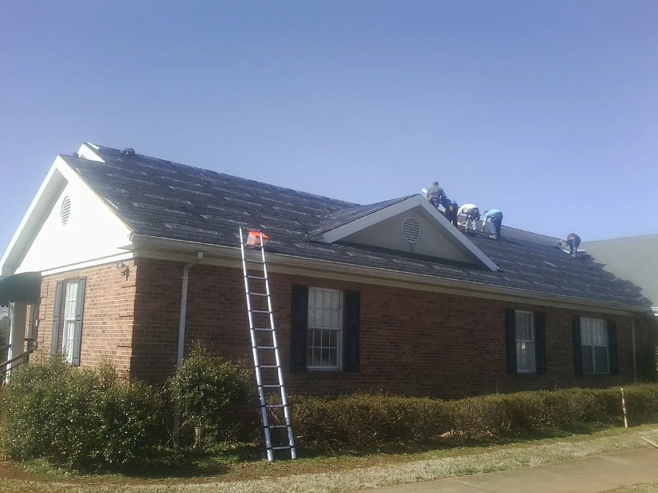 Crew tearing shingles off a brick ranch roof with a ladder set — Emergency Roof Repair work by our crew in Duson