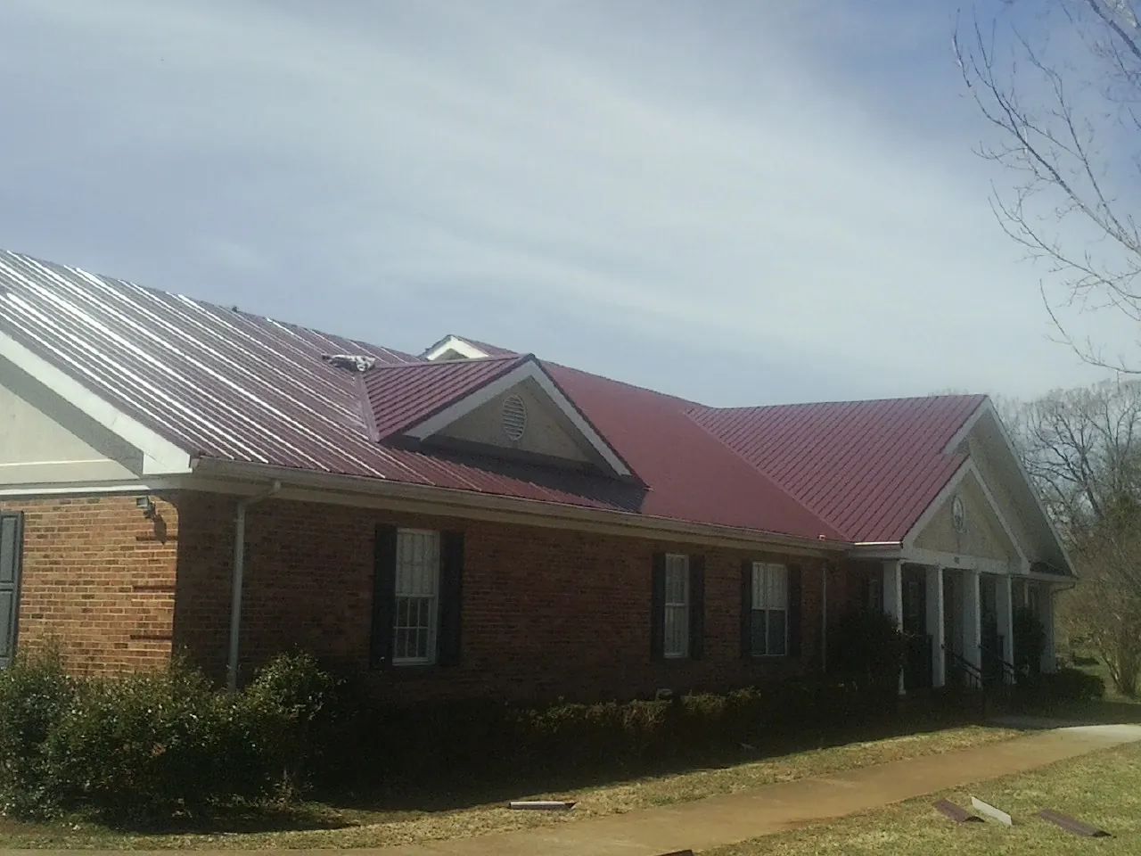 Red metal roof with gabled entries on a long brick building, from a Hail Damage Roof Repair job in Duson