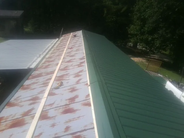 Old rusted panels beside newly installed green metal roofing — Wind Damage Roof Repair by Roofing Brothers in Duson