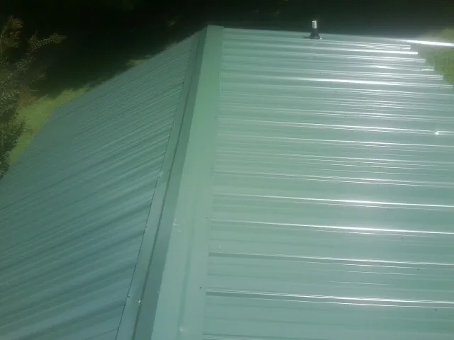 New green metal panels meeting at the ridge of a roof — Flat Roof Repair work by our crew in Duson