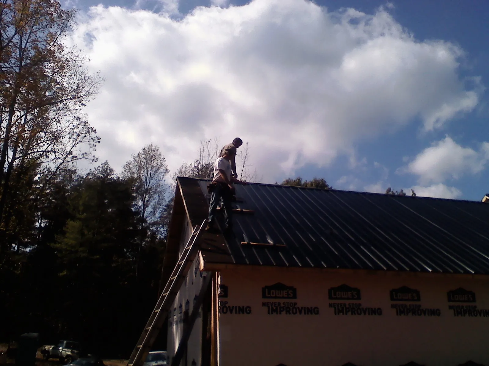 Roofer fastening dark metal panels high against a cloudy sky, from a Roof Inspection job in Duson